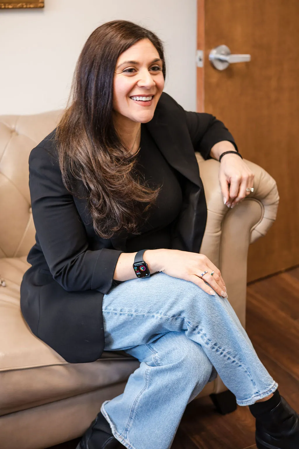 Lindsey Capelli, owner of Living Well Counseling Center, and Licensed Therapist in a black and white polka dot dress sitting at a decorative black table with floral designs holding eyeglasses.