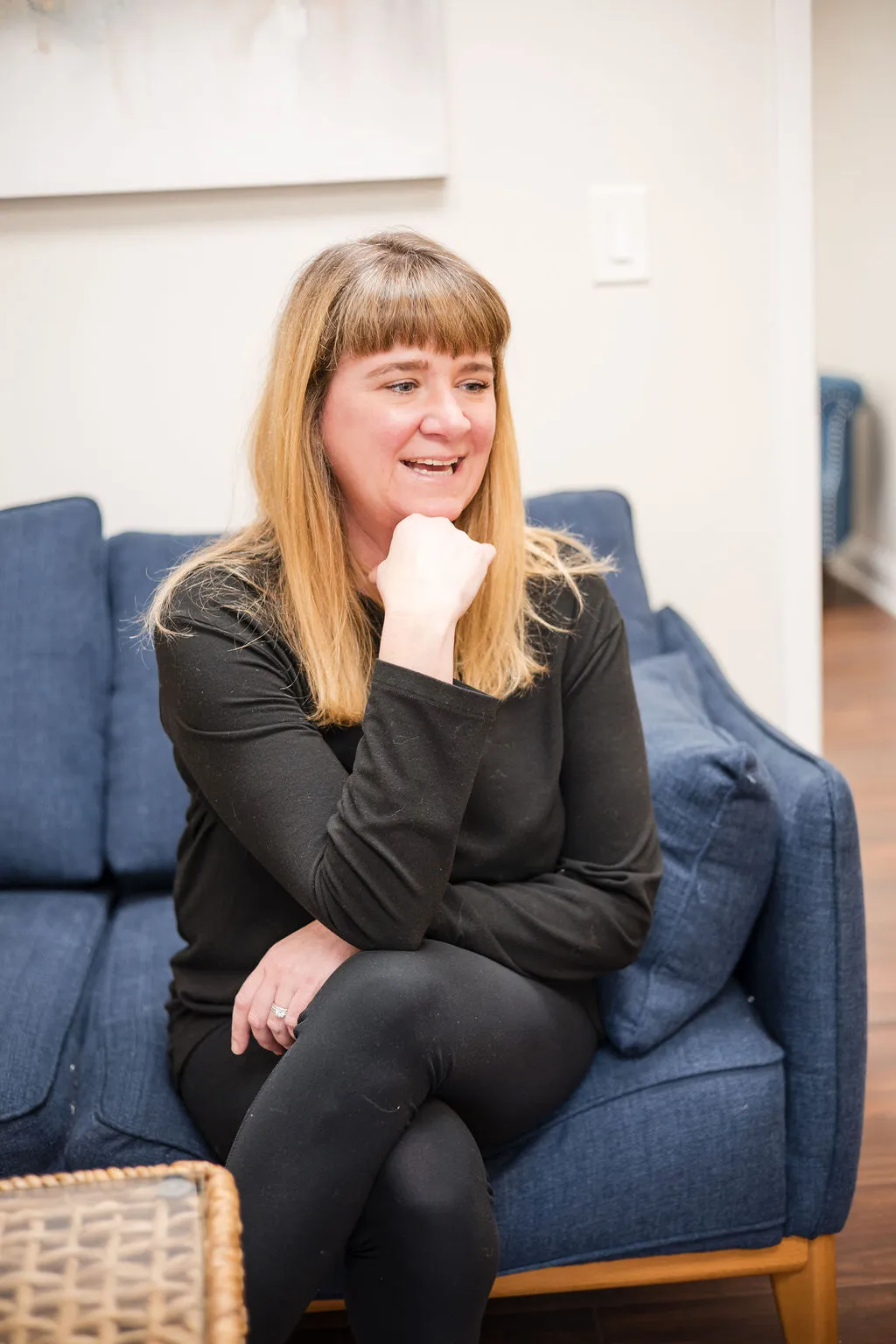 Lindsay Thomson Neill, therapist provider, sitting on a blue couch, smiling and resting her chin on her hand.