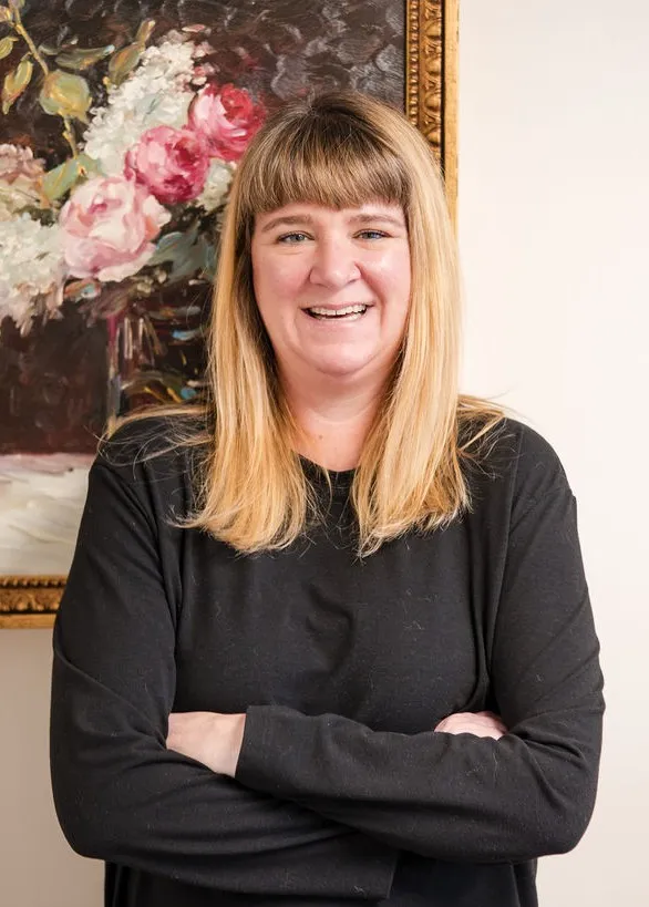 Lindsey Capelli, owner of Living Well Counseling Center, and Licensed Therapist in a black and white polka dot dress sitting at a decorative black table with floral designs holding eyeglasses.
