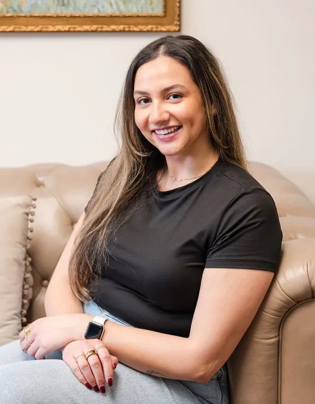 Lindsey Capelli, owner of Living Well Counseling Center, and Licensed Therapist in a black and white polka dot dress sitting at a decorative black table with floral designs holding eyeglasses.
